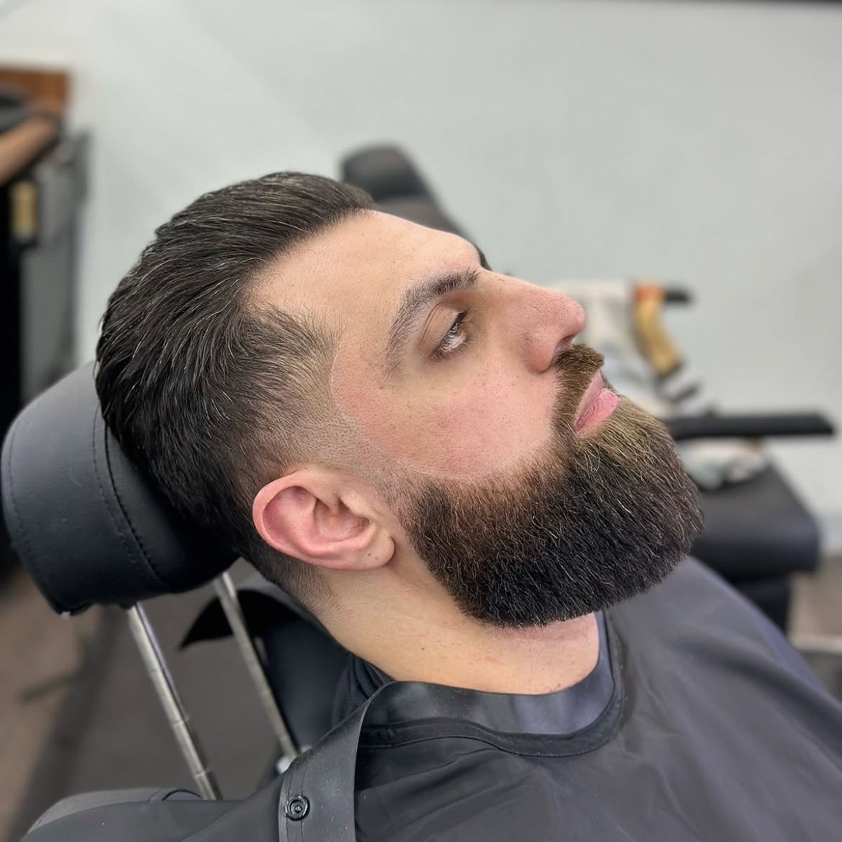 A barber sculpting a client's beard by the front window of Slick Fades in North Olmsted